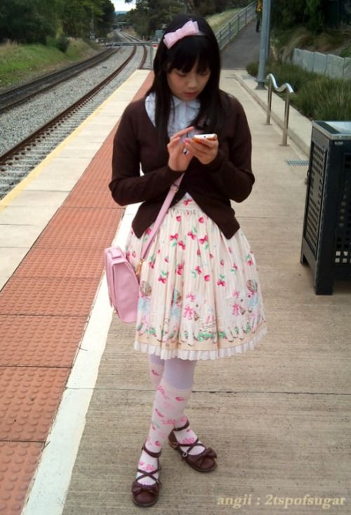 A sweet Lolita in brown, cream, pink and blue looking at her phone